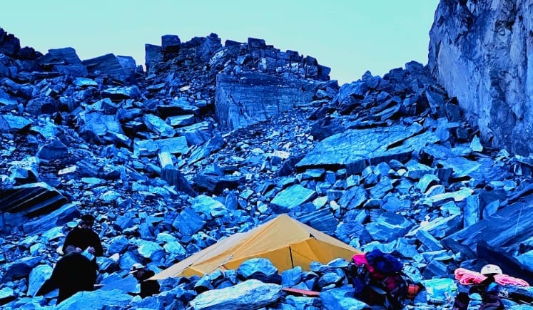 Yellow tent pitched among blue-tinted rocks at an alpine campsite